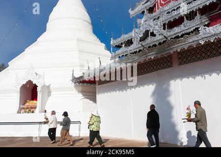 Pellegrini buddisti asiatici che camminano con mazzo di fiori intorno all'antica pagoda di Wat Phrathat Doi Kong Mu, Mae Hong son, Thailandia. Foto Stock