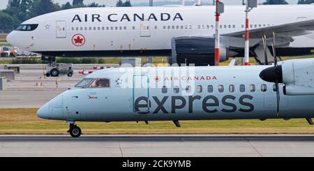 Richmond, British Columbia, Canada. 31 luglio 2020. Un aereo di linea regionale Air Canada Express Dash 8 (C-GGMN) atterra all'aeroporto internazionale di Vancouver. L'aereo è gestito sotto contratto per Air Canada da Jazz Aviation, una filiale di Chorus Aviation. In background è un Air Canada Boeing 777-200LR (C-FNNH) getto messo in deposito a causa della pandemia COVID-19 e conseguente grave recessione nel viaggio aereo. Credit: Bayne Stanley/ZUMA Wire/Alamy Live News Foto Stock