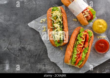 Hot dog con vari riempimenti. Sfondo scuro. Cibo sfondo con spazio di copia. Vista dall'alto. Hot dog con senape e ketchup, lattuga, formaggio e. Foto Stock