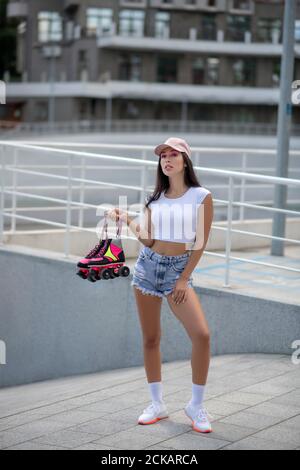 Bella ragazza in shorts e top holding pattini a rotelle Foto Stock