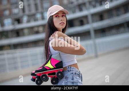 Bella ragazza in cappello che porta pattini a rotelle in mani Foto Stock