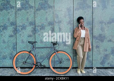 Giovane donna africana che parla sul telefono cellulare mentre si sta in piedi vicino la sua moto in città Foto Stock