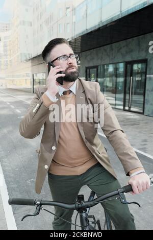 Uomo maturo che parla sul telefono cellulare mentre si guida su un in bicicletta in città Foto Stock