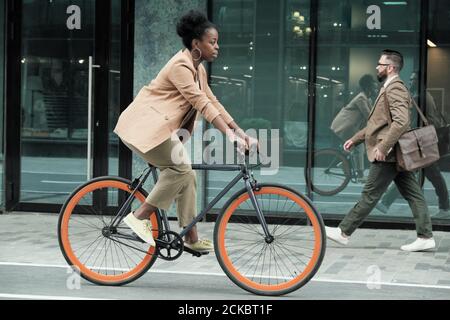 Giovane donna africana che cavalcano in bicicletta per il suo lavoro lungo le strade della città Foto Stock