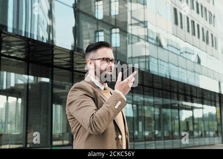Uomo d'affari con cuscinetti maturi che parla sul telefono cellulare mentre si sta in piedi la città Foto Stock