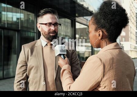 Donna africana con microfono che intervistano l'uomo mentre si levano in piedi in città Foto Stock