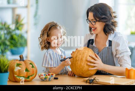 Felice famiglia che si prepara per Halloween. Madre e bambino che intagliano le zucche a casa. Foto Stock