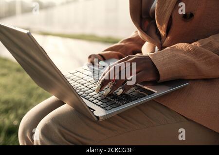 Primo piano di una donna d'affari che si siede all'aperto con un computer portatile in ginocchio e lavorare online Foto Stock