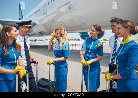 Bei assistenti di volo e bei piloti che parlano e sorridono mentre in piedi vicino all'aereo Foto Stock