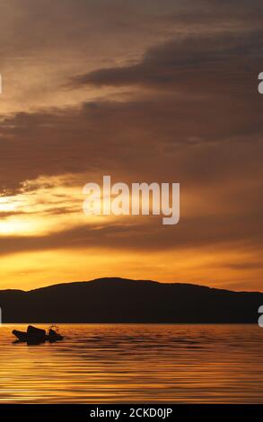 Tramonto a Carsaig Bay, Tayvallich, Argyll, Scozia con la silhouette di una piccola barca a motore in primo piano e che si affaccia sul Sound of Jura a Jura Foto Stock