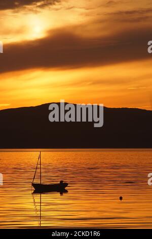Tramonto a Carsaig Bay, Tayvallich, Argyll, Scozia con la silhouette di un piccolo yacht in primo piano e che si affaccia sul Sound of Jura a Jura Foto Stock