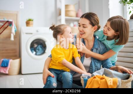 Bella giovane donna e bambino ragazza piccolo helper stanno divertendosi e sorridendo mentre facendo lavanderia a casa. Foto Stock