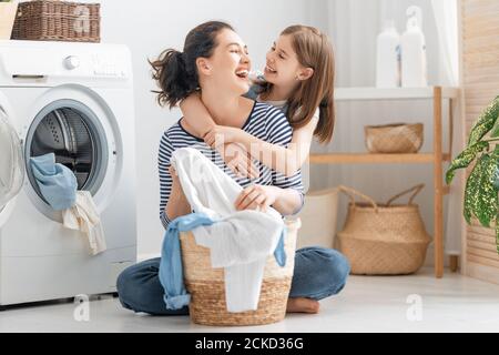 Bella giovane donna e bambino ragazza piccolo helper stanno divertendosi e sorridendo mentre facendo lavanderia a casa. Foto Stock