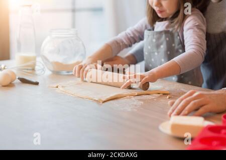 Padre e figlia che arrotolano l'impasto in cucina per fare biscotti, tagliati Foto Stock