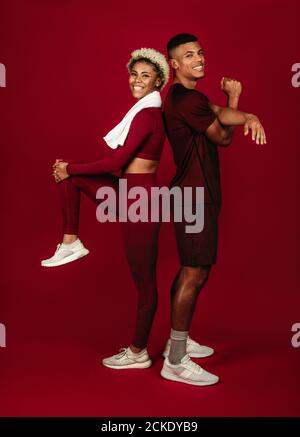 Sorridente afroamericano fitness coppia in piedi insieme su sfondo maroon. Coppia facendo esercizi di riscaldamento insieme. Foto Stock