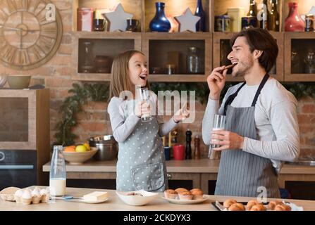 Papà allegro e figlia piccola mangiare biscotti e bere latte in cucina Foto Stock