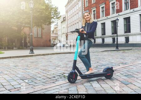 trasporti ecologici - giovani e belle donne d'affari passeggiate scooter elettrico nelle strade della città Foto Stock