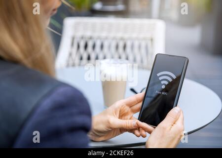 area wi-fi gratuita - donna che collega il telefono al pubblico rete wireless al bar Foto Stock