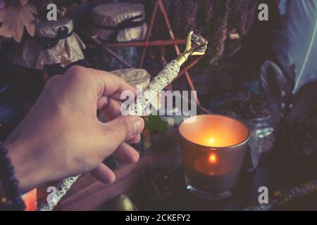 La mano della donna sta tenendo la bacchetta magica che esegue un rituale della strega pagana. Tinta a colori freddi Foto Stock