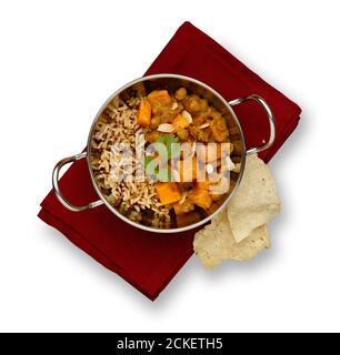 Piatto tradizionale blati con delizioso curry di pollo vegetale e riso rustico, guarnito con un filo di corriandolo, su un tovagliolo rosso e popa Foto Stock
