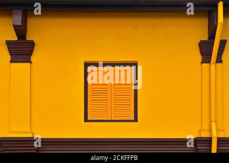 Una serranda veneziana chiusa in legno isolata su una parete dipinta di giallo. Contrastato da architrave marrone e colonne. Foto Stock