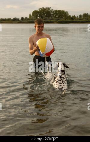 Un giovane gioca con un cane dalmata nel acqua Foto Stock