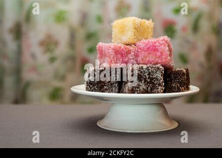 Primo piano del colorato dessert australiano Lamingtons accatastato e servito su una base per torte Foto Stock