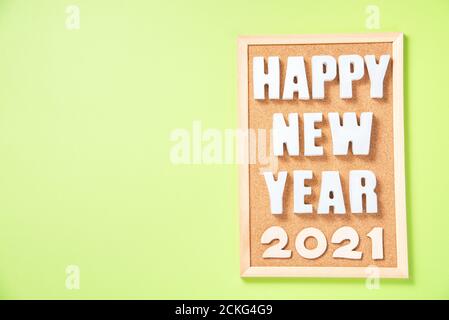 Iscrizione con lettere in gesso Felice anno nuovo su un corkboard e numeri 2021 su sfondo verde vista dall'alto con posizione per il testo Foto Stock