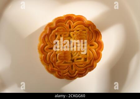 Traduzione della pasta di semi cinese in inglese-loto con yolk-tradizionale mooncake su un piatto con luce solare vicino a una finestra no logo o marchio Foto Stock