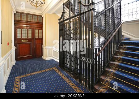 Un tradizionale ascensore a gabbia in metallo nel vano delle scale di un blocco di appartamenti nel centro di Londra. Ristrutturato di recente, presenta nuovi tappeti, scale e porte decorate Foto Stock