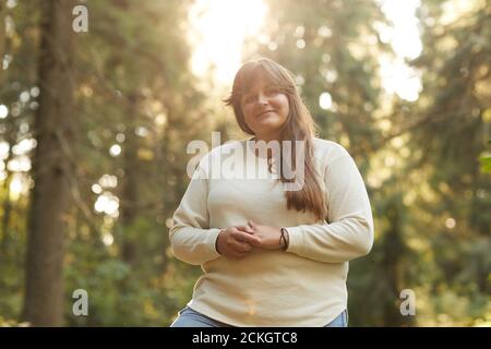 Ritratto di giovane donna in sovrappeso che sorride alla fotocamera mentre si è in piedi all'aperto Foto Stock