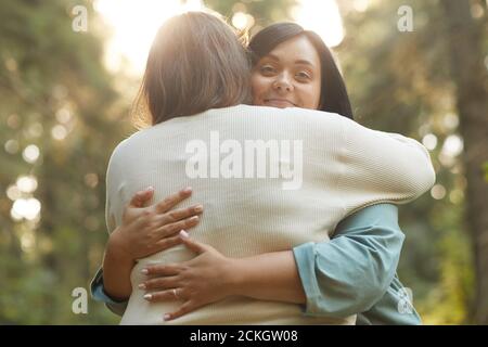 Ritratto di giovane donna che guarda la macchina fotografica mentre la abbraccia fidanzata si levano in piedi all'aperto Foto Stock