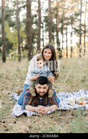 Famiglia, persone, amore e felicità concetto. Ritratto esterno di giovane attraente famiglia, papà, mamma e figlio di capretto, sdraiato sulla coperta a scacchi dentro Foto Stock