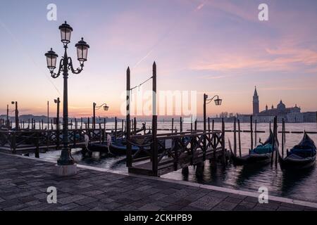 Una lampada sul lungomare di Riva degli Schiavoni con gondole ormeggiate e la basilica di San Giorgio maggiore sullo sfondo durante un alba a Venezia, esso Foto Stock