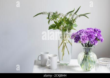 Bouquet nuziale di garofani lilla in quattro vasi rotondi di vetro di diverse dimensioni come decorazione della tavola. Due tazze bianche. Foto Stock