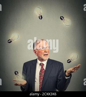 Ritratto felice dirigente di uomo d'affari senior in giocoleria vestito giocare con lampadine isolate su sfondo grigio della parete dell'ufficio Foto Stock