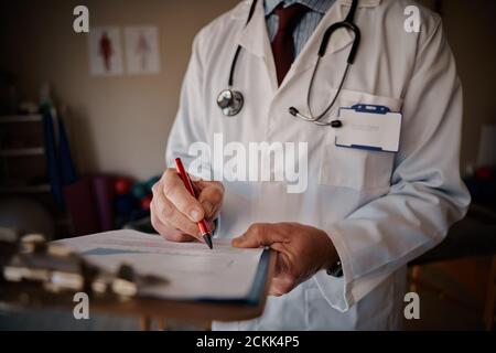 Primo piano del medico maschile senior che scrive note sulla clipboard in ospedale - scritto medico Foto Stock