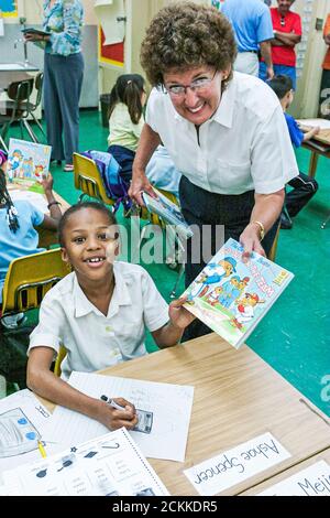 Miami Florida, Frederick Douglass Elementary School, quartiere a basso reddito, studentessa nera ragazza legge dipendente dando donare libro donna in classe Foto Stock