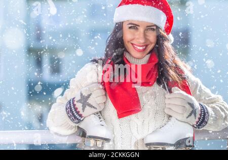 Donna in un cappello rosso di Natale e sciarpa, maglione bianco e guanti tiene pattini di ghiaccio attraverso il suo collo. Foto Stock