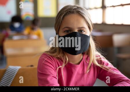 Ritratto di ragazza che indossa maschera seduta in classe a scuola Foto Stock