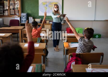 Vista posteriore di ragazzo che alza la mano nella classe a scuola Foto Stock