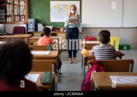 Insegnante di sesso femminile che indossa maschera di insegnamento in classe a scuola Foto Stock