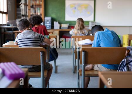Vista posteriore del gruppo di bambini che studiano mentre si siedono la scrivania a scuola Foto Stock