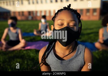 Ragazza che indossa la maschera facciale che esegue yoga in giardino Foto Stock