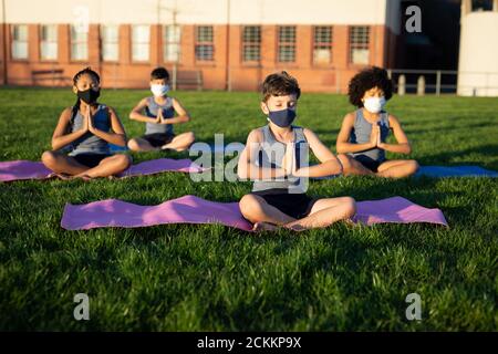 Gruppo di bambini che indossano maschere per il viso che eseguono yoga nella giardino Foto Stock