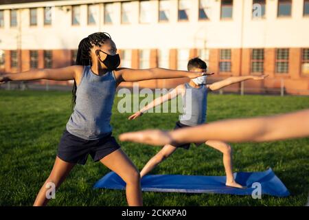 Ragazza che indossa la maschera facciale che esegue yoga in giardino Foto Stock