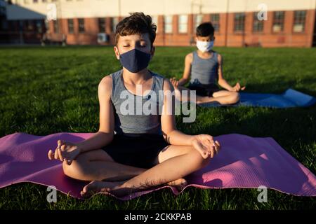 Ragazzo che indossa la maschera facciale che esegue yoga in giardino Foto Stock