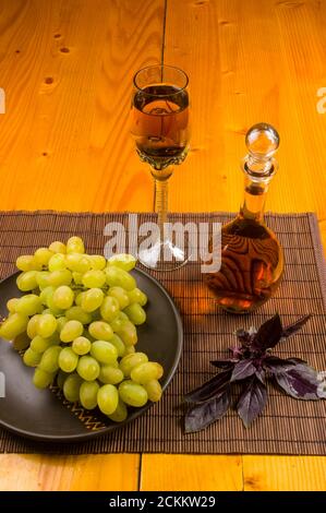 grande spazzola di uva verde in un piatto di ceramica, un decanter e un bicchiere di vino e formaggio Foto Stock