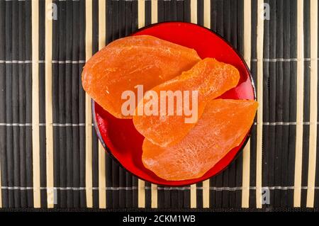 Fette di mango essiccato in un piatto rosso su un tappetino di bambù, guardaroba. Foto Stock