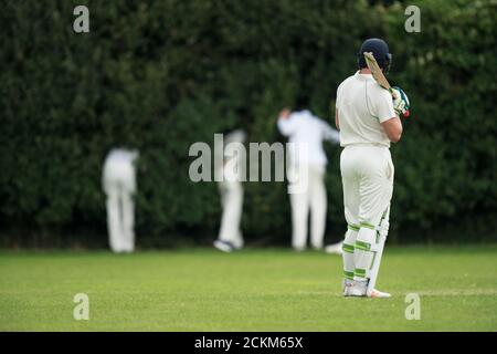 Cricket batsman in attesa dei fielder di trovare la palla che ha colpito per sei. Foto Stock